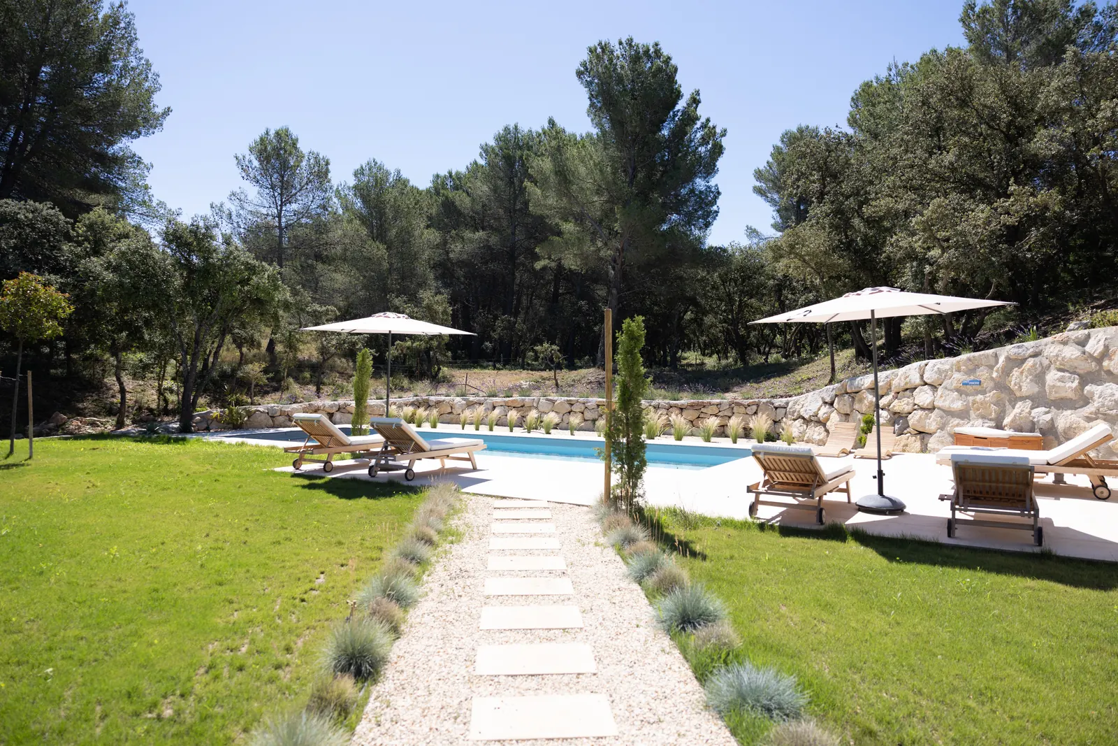 L'allée pavée du jardin sud mène à la piscine, entre gazon et graminées