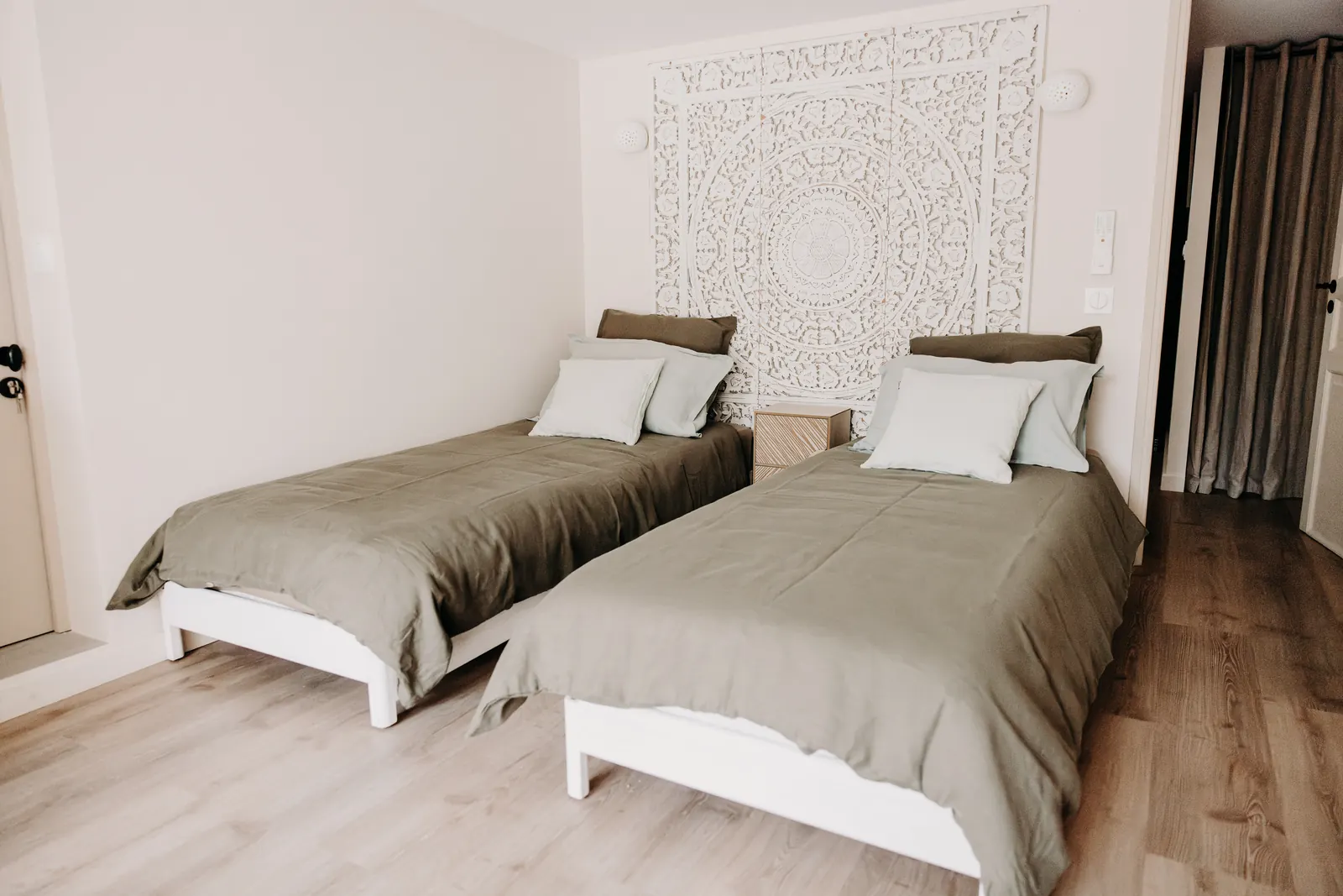 La chambre du rez-de-jardin : deux lits au linge vert olive et tête de lit sculptée