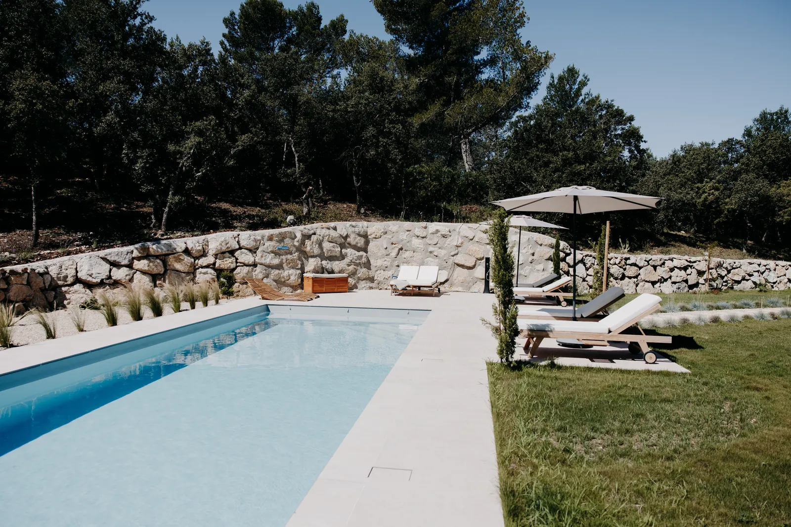 La piscine de 12 × 4 m, ses murets de pierre sèche et ses parasols