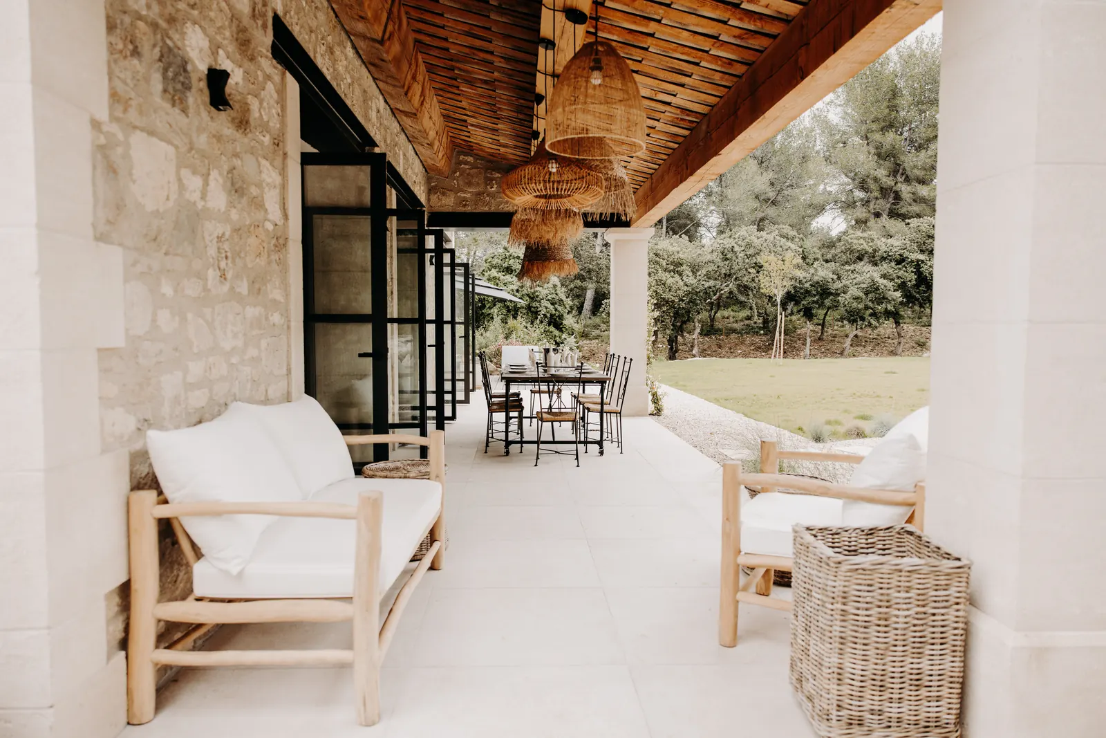 Le salon de la terrasse couverte, fauteuils en bois et coussins clairs