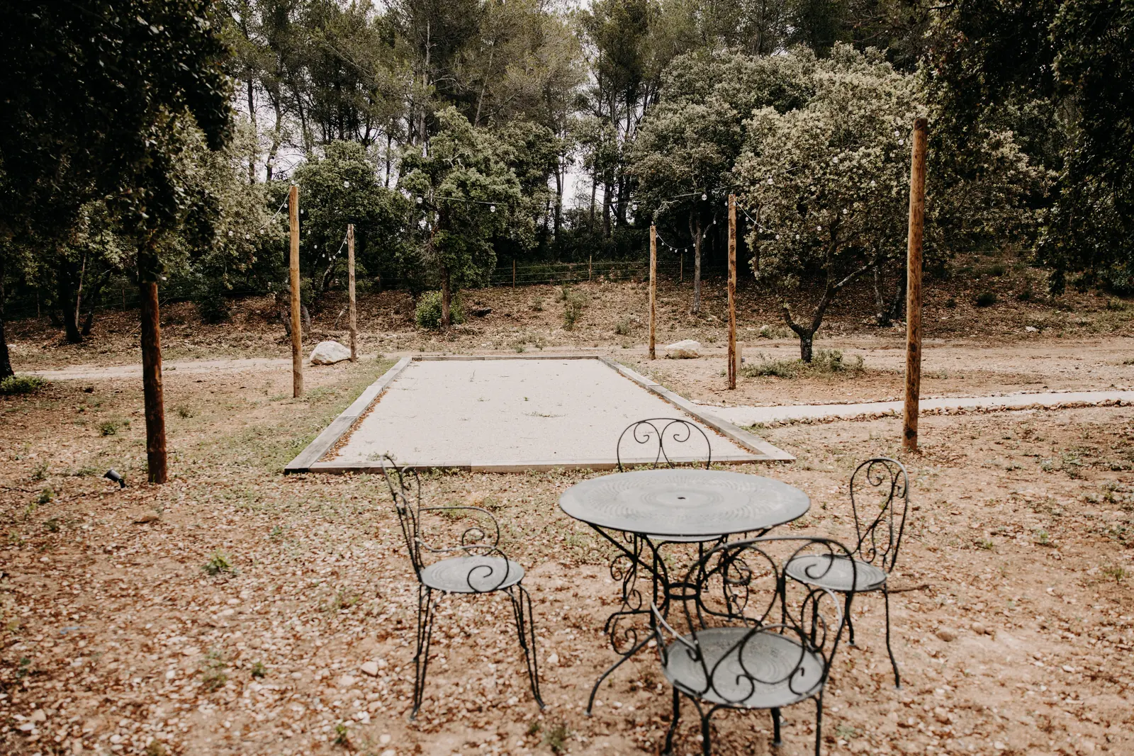 Le terrain de pétanque et sa table en fer forgé dans l'olivaie du jardin nord